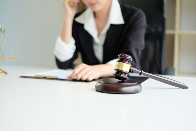 Woman in a suit contemplating while seated at a desk with a gavel nearby.